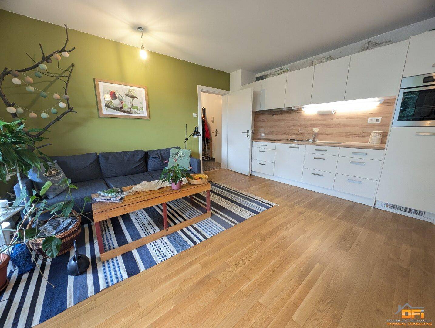 Wohnbereich mit grüner Akzentwand, Sofa und integrierter, moderner Einbauküche.