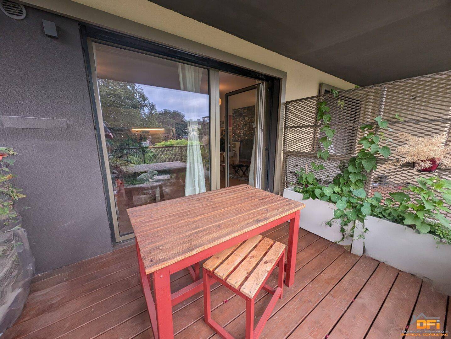 Balkon mit Holzboden und Sitzgelegenheiten, direktem Zugang zum Innenbereich durch eine Schiebetür.