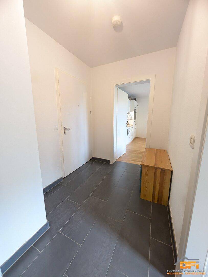 Eingangsbereich mit dunklem Fliesenboden, weiß gestrichenen Wänden und einer Holzbank.