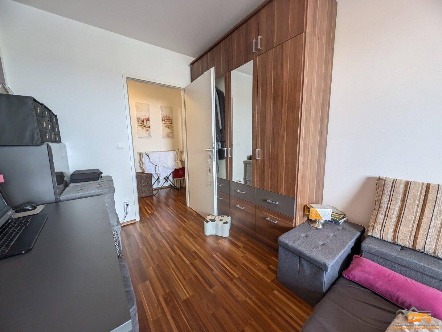Kleines Schlafzimmer oder Gästezimmer mit Holzschrank und Blick in einen angrenzenden Raum.