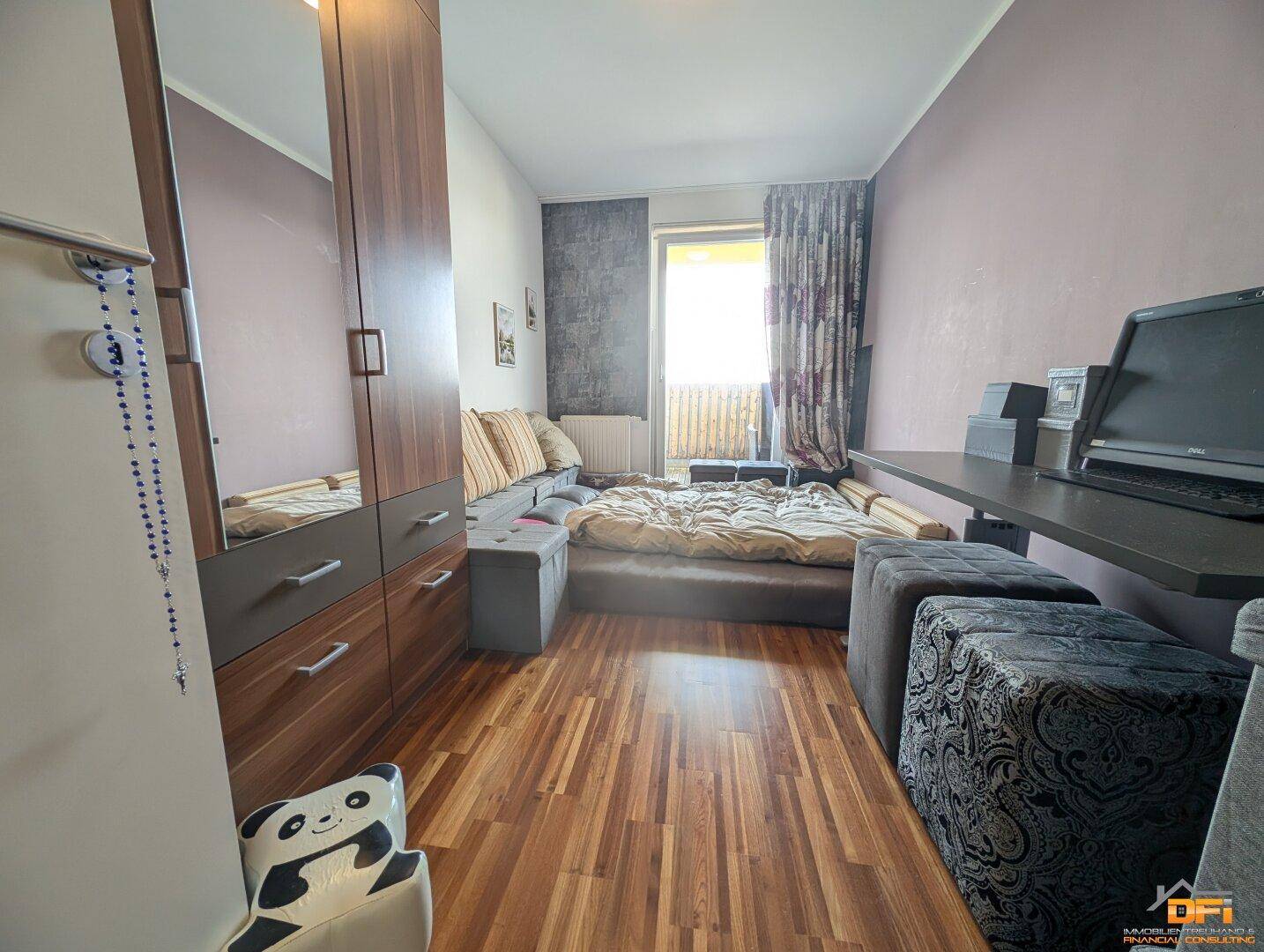 Gemütliches Schlafzimmer mit Bett, Holzschrank und einem Arbeitsbereich am Fenster.