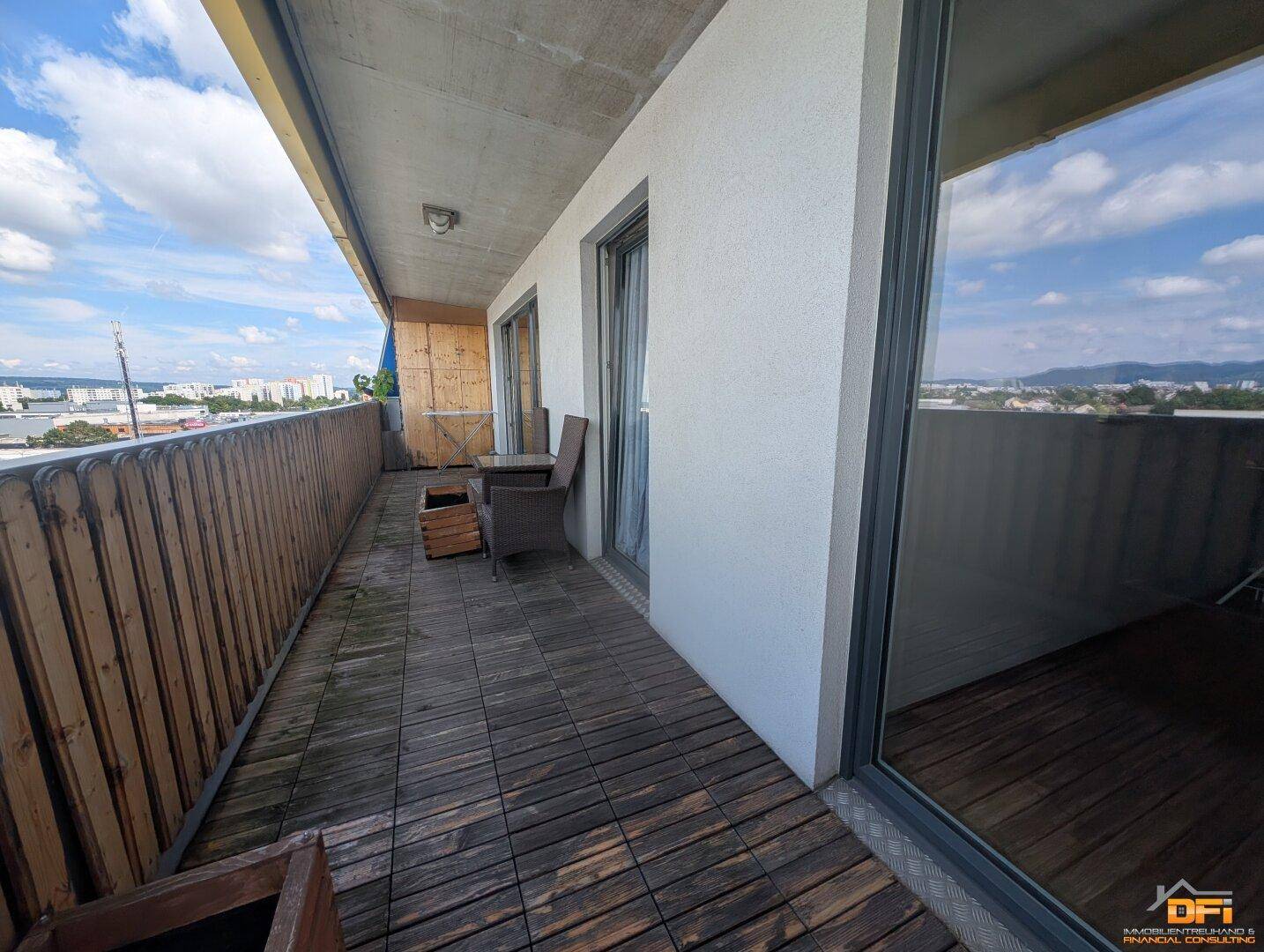 Geräumiger Balkon mit Holzboden und Panoramablick auf die Umgebung und die Stadt.