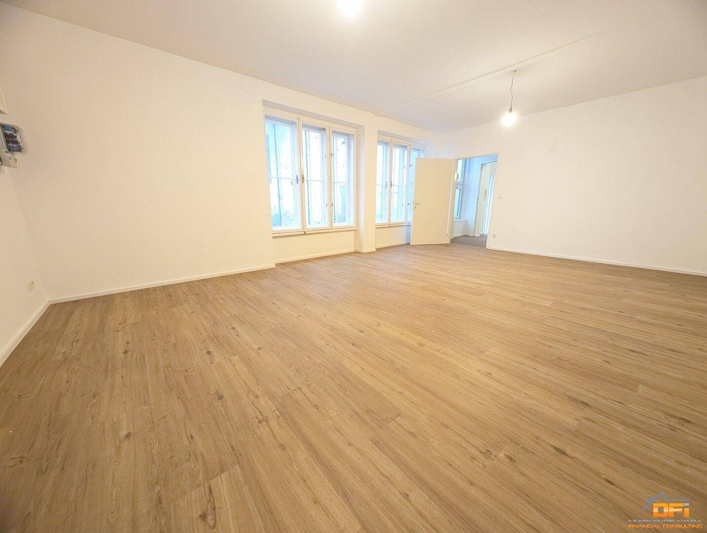 Großzügiger, leerer Raum mit Laminatboden und mehreren Fenstern, bietet viel Tageslicht.
