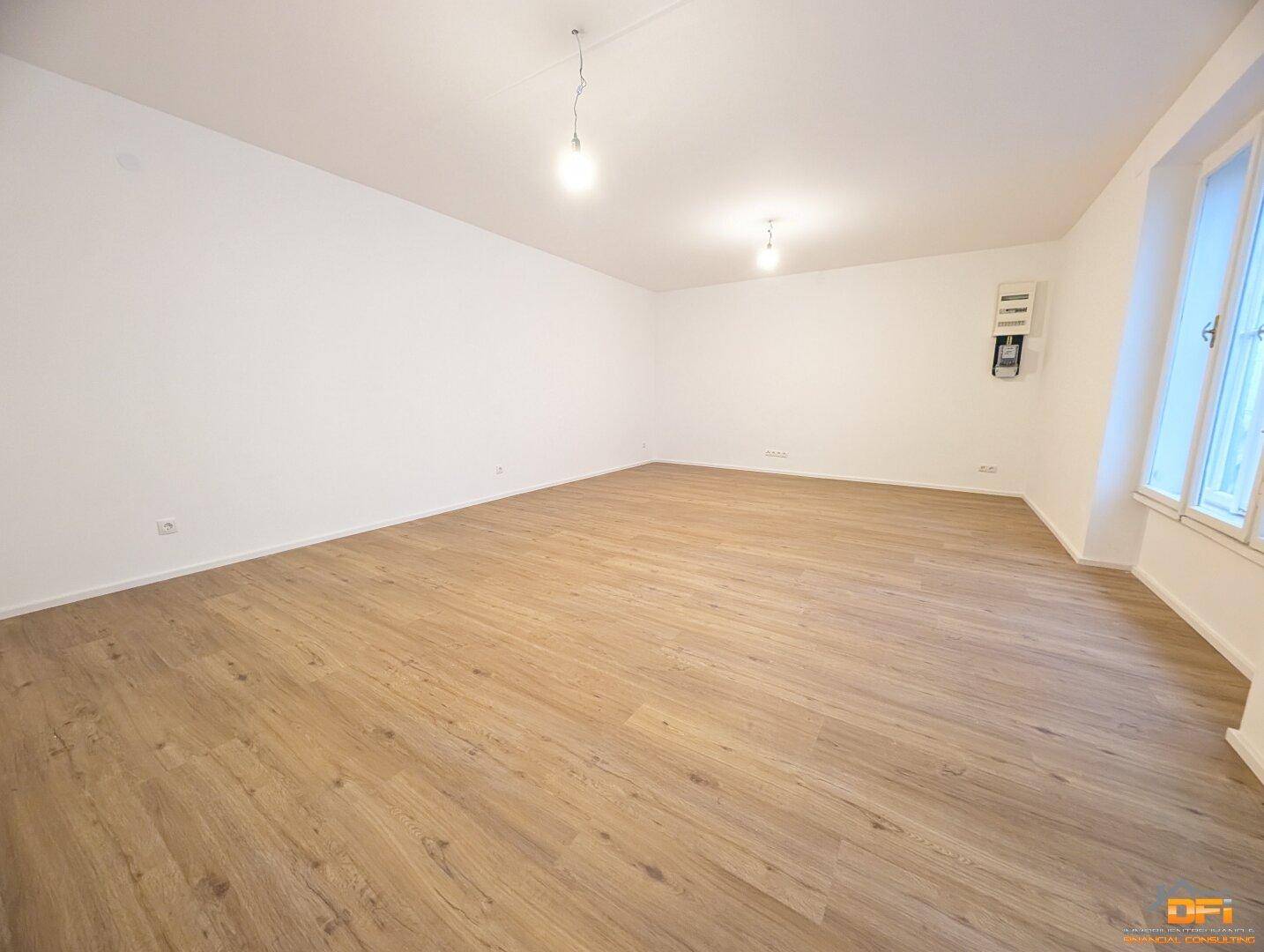 Geräumiger Wohnbereich mit hellem Laminatboden und weißen Wänden, bereit für individuelle Gestaltung.