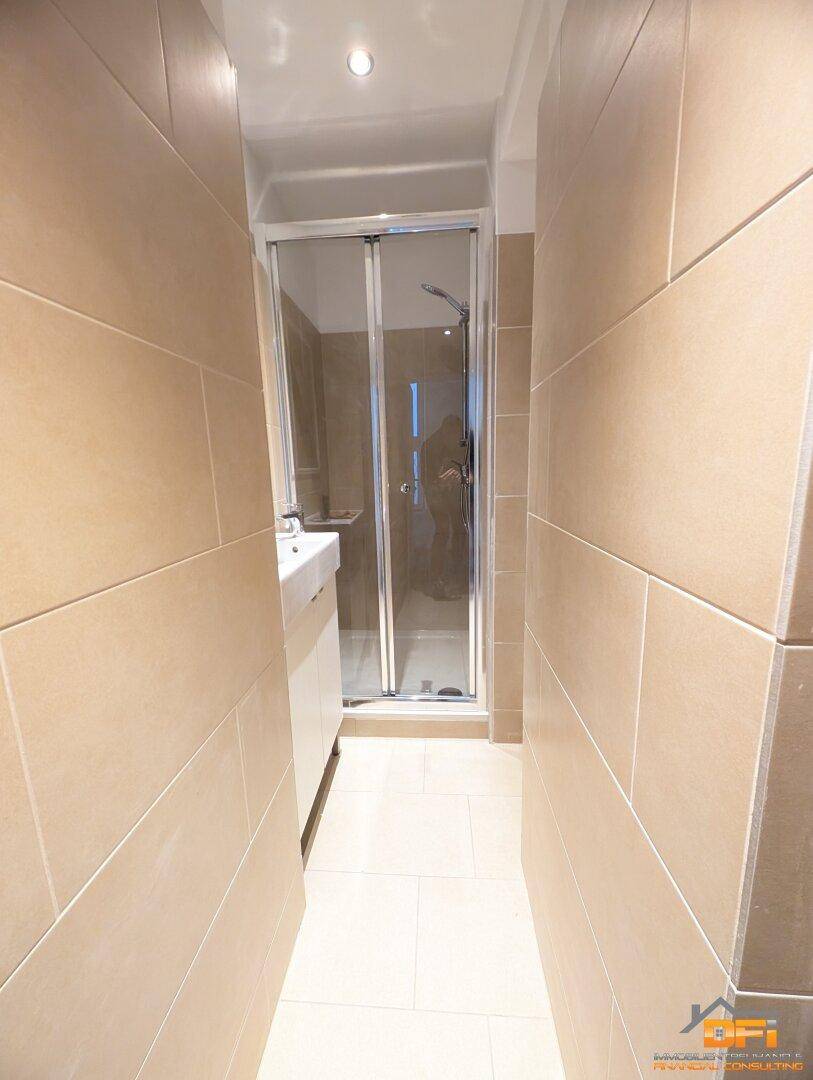Modernes, schmales Badezimmer mit Duschkabine, Waschbecken und beigefarbenen Fliesen.