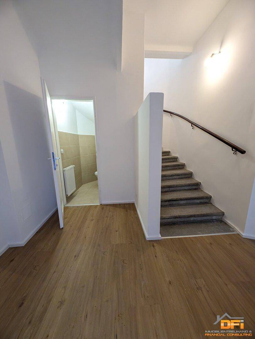 Heller Flur mit Holz-Laminatboden, Treppe und Zugang zu einem Badezimmer.