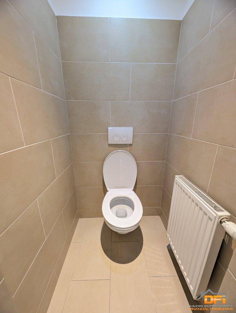 Einfaches WC mit Wand-WC und Heizkörper, gefliest in neutralem Beige.