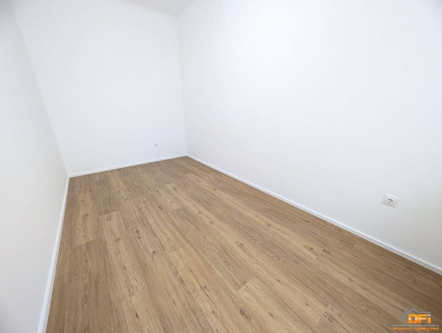 Leeres Zimmer mit Laminatboden und weißen Wänden, vielseitig als Schlaf- oder Arbeitszimmer nutzbar.
