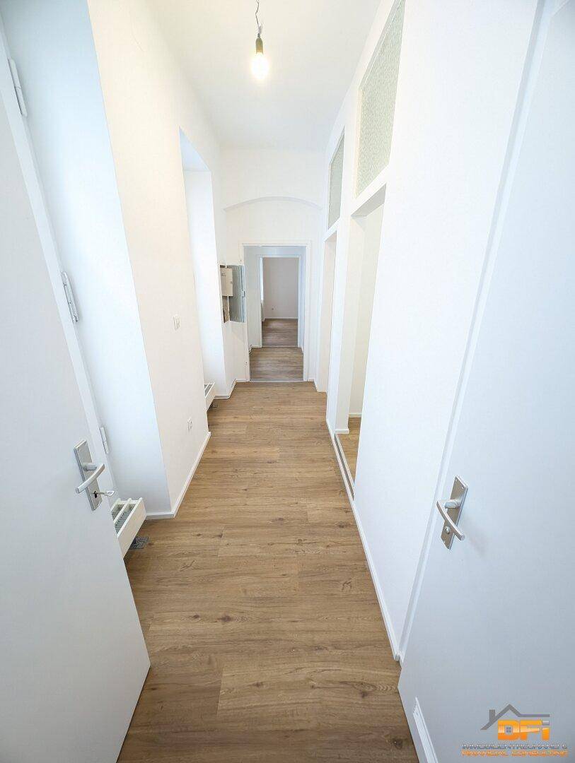 Heller Flur mit Laminatboden und weißen Wänden, der zu weiteren Räumen führt.