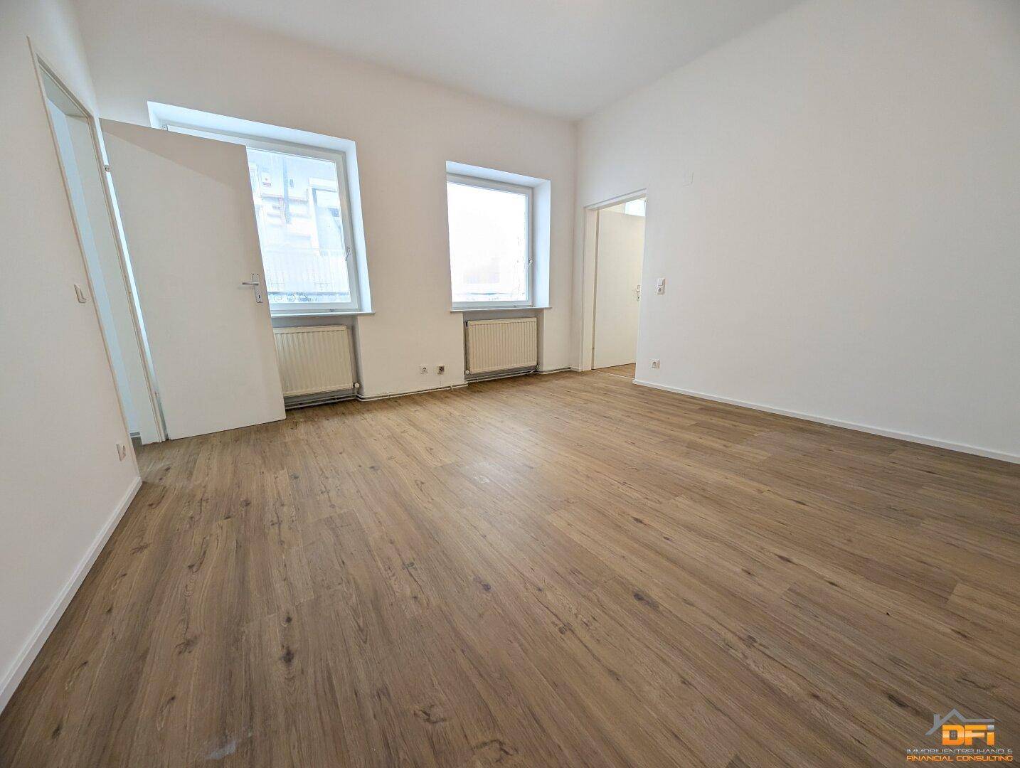 Geräumiges Zimmer mit Laminatboden und großen Fenstern, ideal als Wohnbereich.