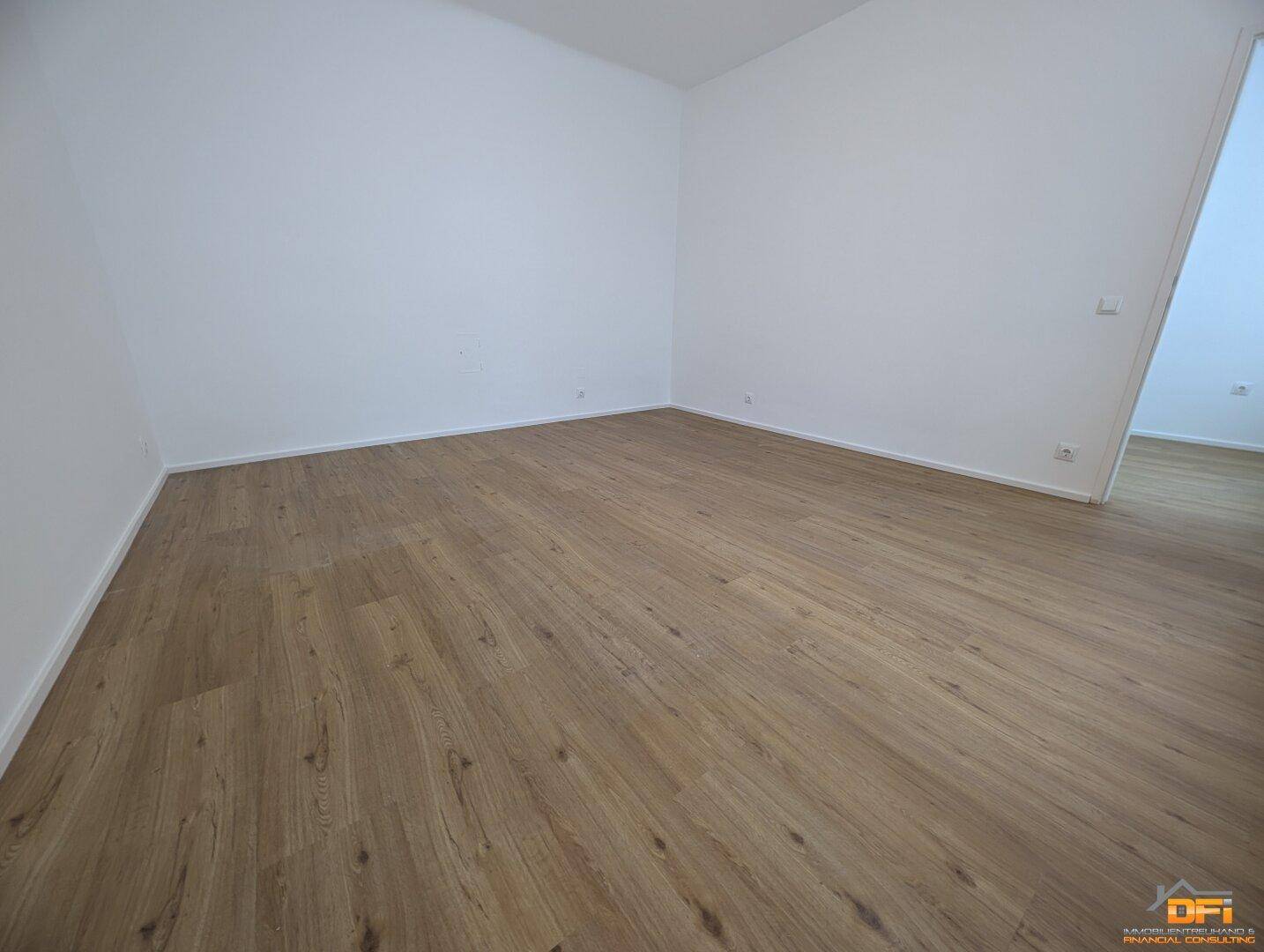 Leeres Zimmer mit Laminatboden und weißen Wänden, bereit für individuelle Einrichtung.