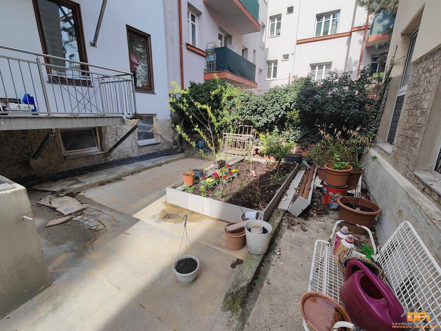 Kleiner Hinterhofgarten mit Hochbeeten und Topfpflanzen, umgeben von Gebäuden.