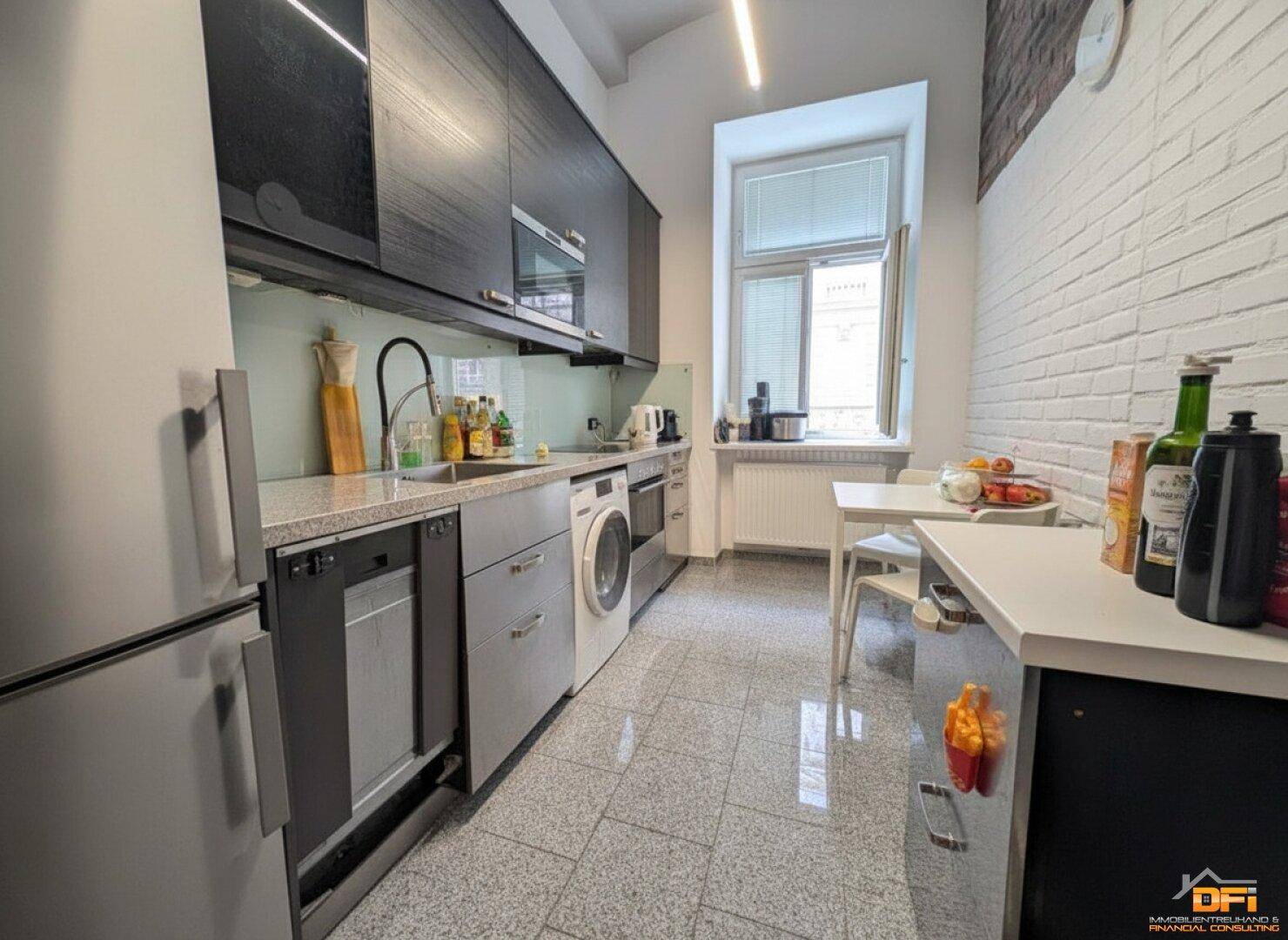 Moderne Küche mit dunklen Oberschränken, hellen Arbeitsplatten und einem kleinen Essbereich am Fenster.