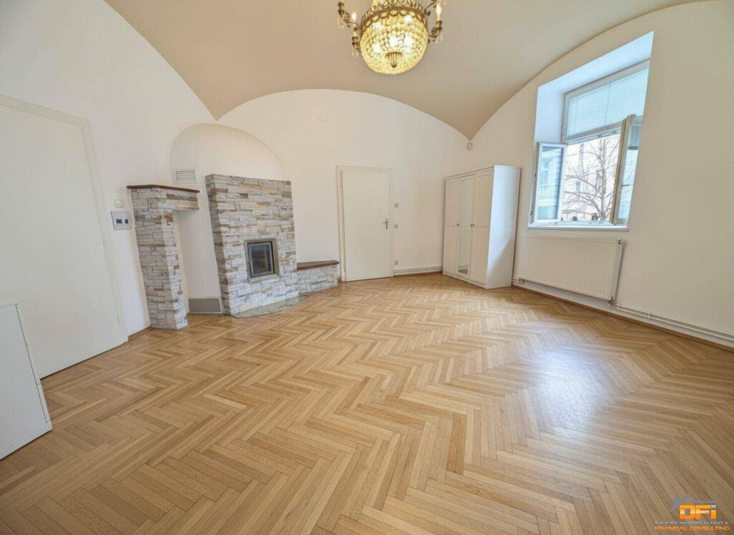 Heller Raum mit Fischgrätparkett, gewölbter Decke und einem Kamin als zentrales Element.