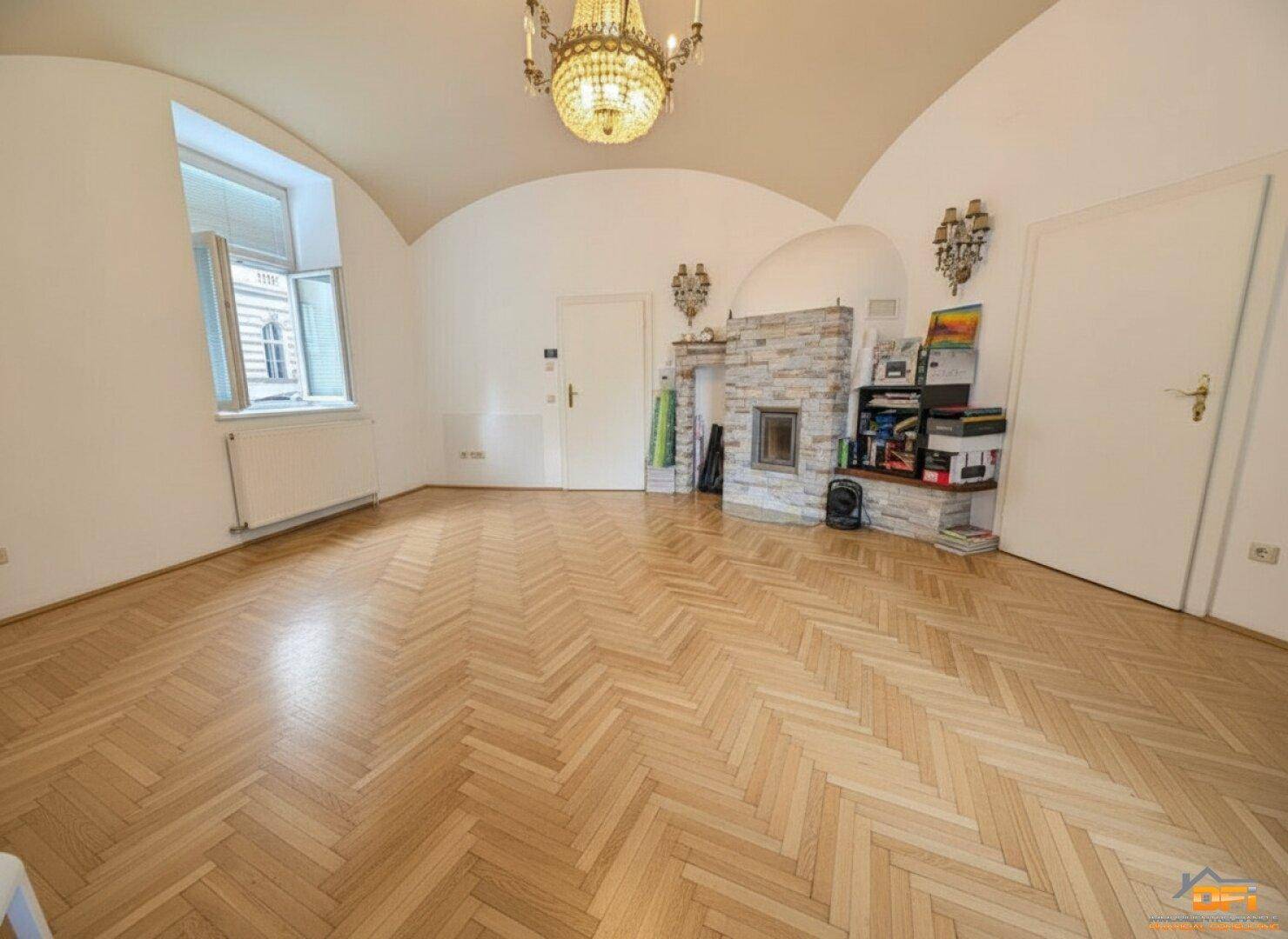 Geräumiges Wohnzimmer mit elegantem Fischgrätparkett, Kamin und dekorativen Wandleuchten.