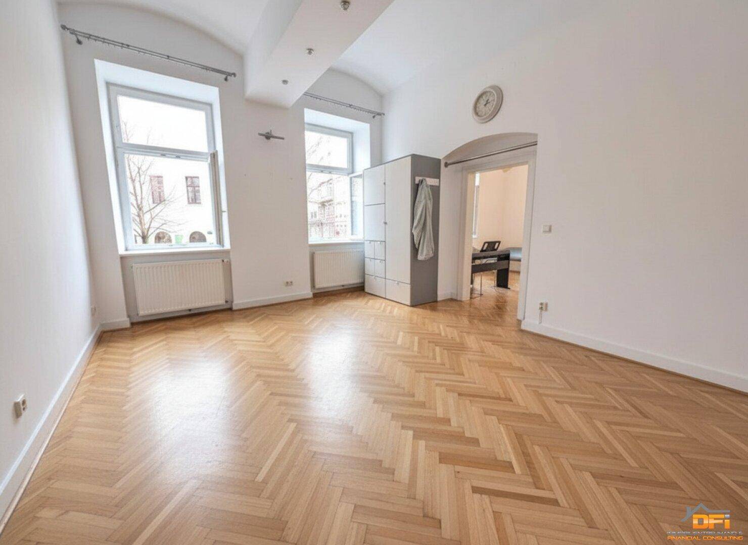 Heller Wohnraum mit Fischgrätparkett, gewölbter Decke und zwei großen Fenstern mit Blick nach draußen.