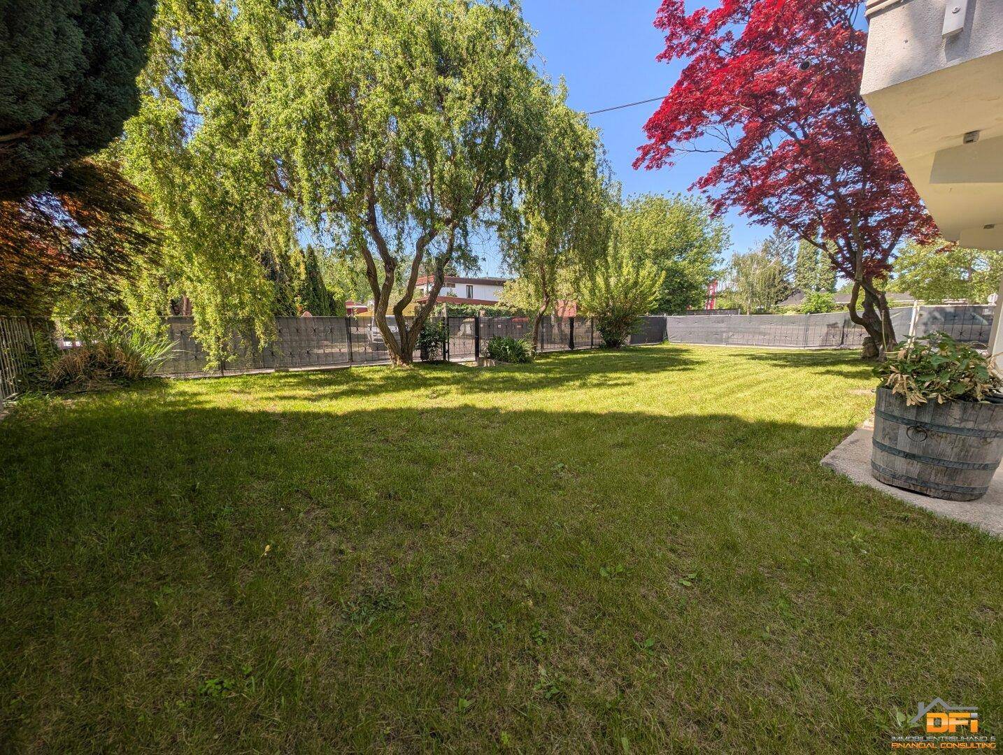 Großer, sonniger Garten mit gepflegtem Rasen und hohen Bäumen im Hintergrund.