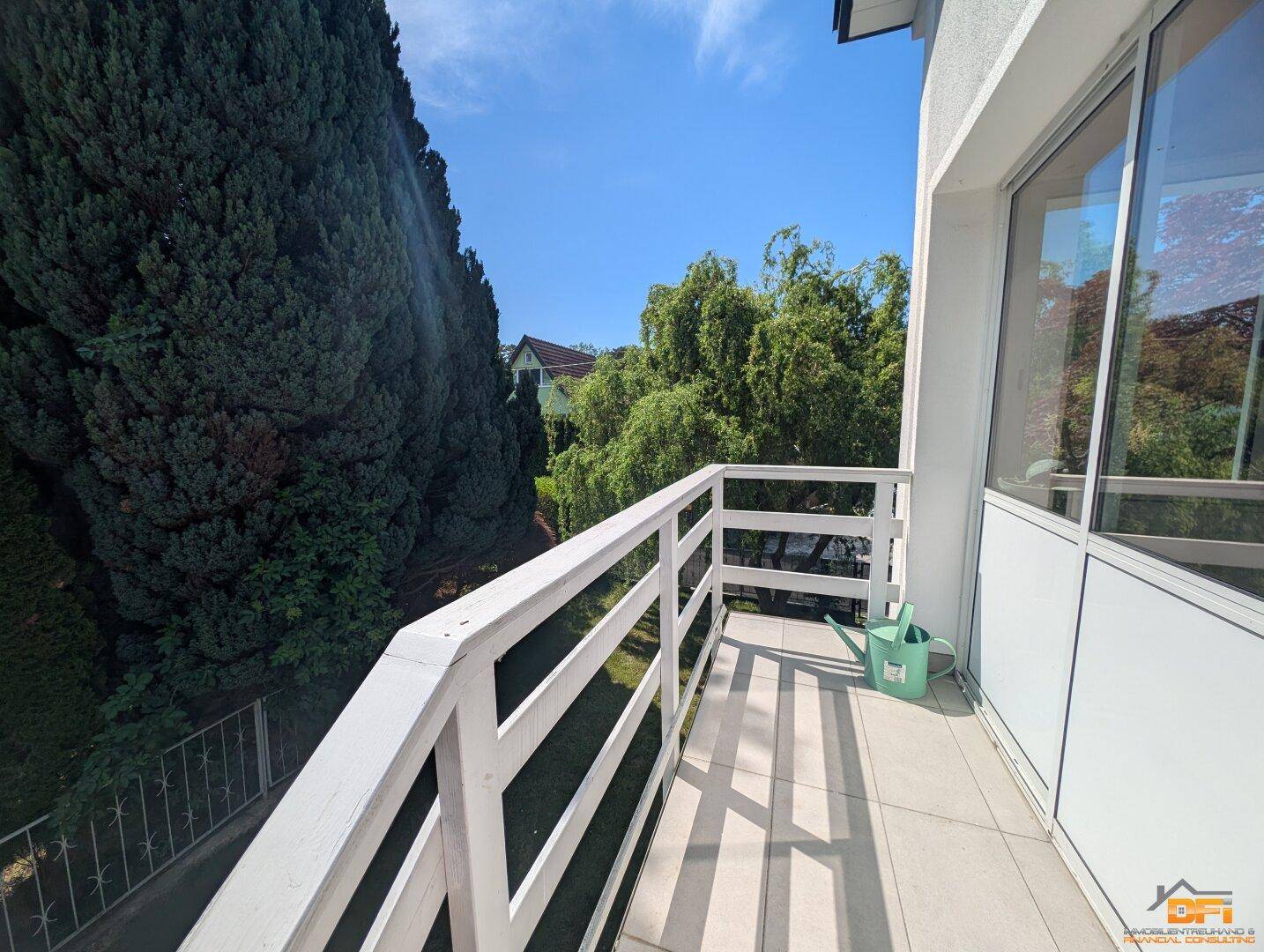 Kleiner Balkon mit weißem Geländer und Blick ins Grüne.