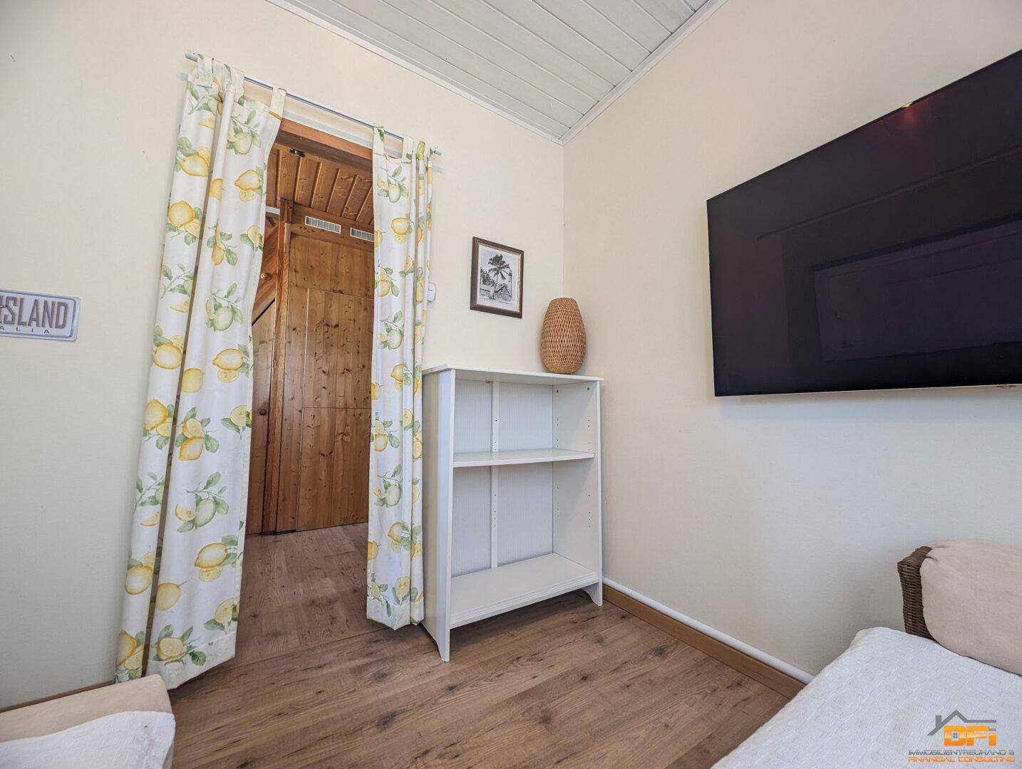 Heller Wohnraum mit Holzboden, Regal und Zugang zu einem weiteren Zimmer.
