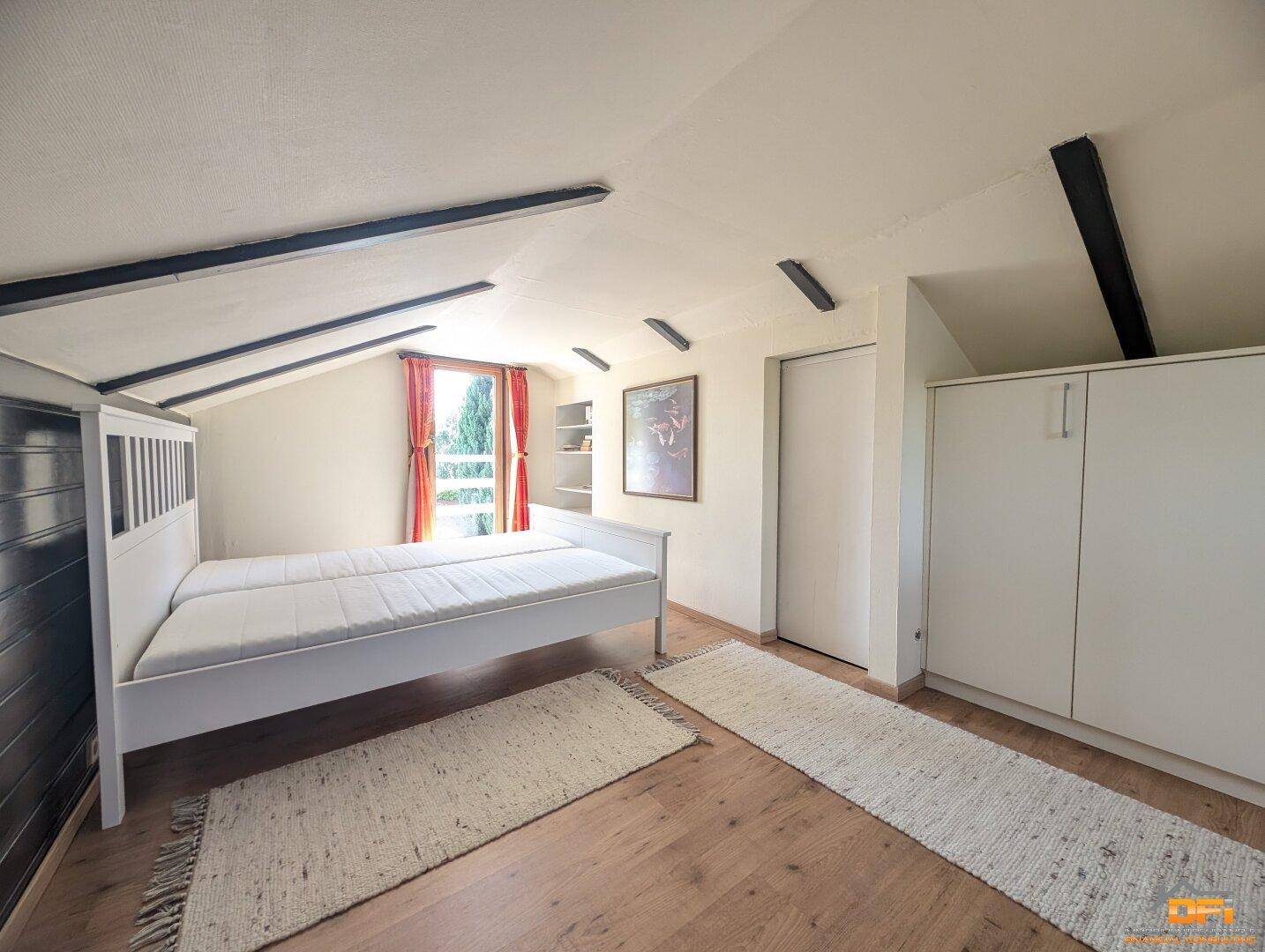 Schlafzimmer im Dachgeschoss mit Doppelbett, Holzbalken und Einbauschränken.
