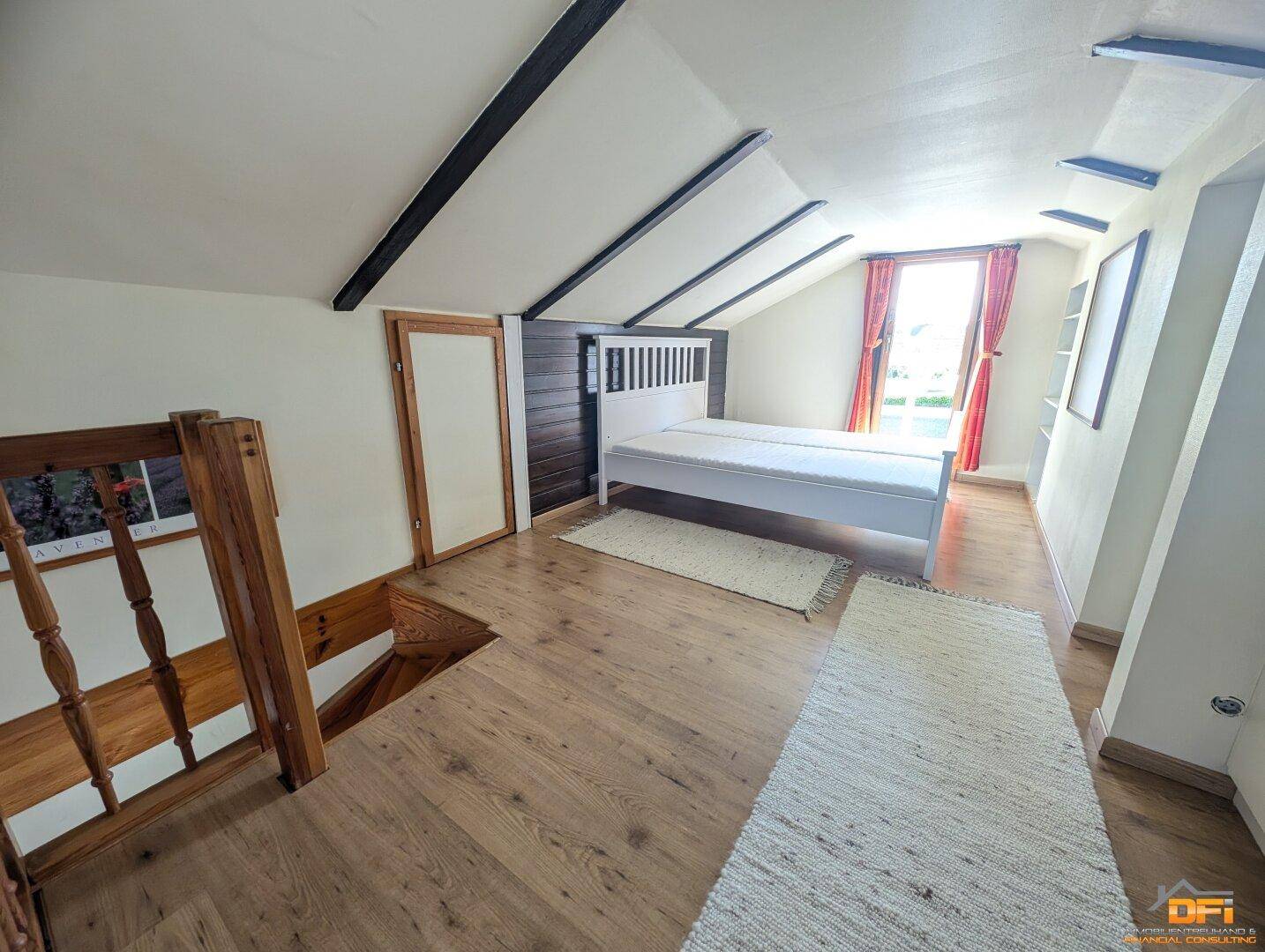 Dachgeschoss-Schlafzimmer mit Holzboden, Bett und Blick auf die Treppe.
