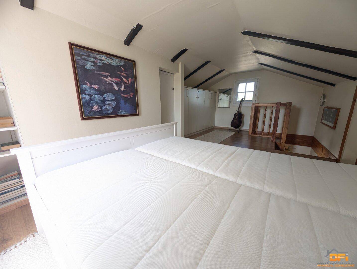 Helles Schlafzimmer im Dachgeschoss mit Doppelbett, Holzbalken und Fenster.