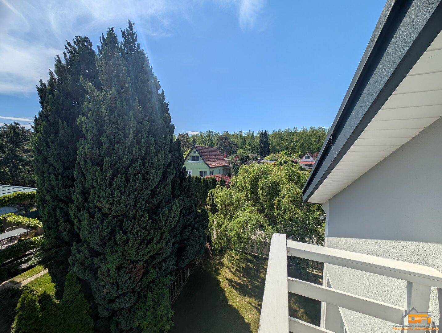 Weitläufiger Blick vom Balkon auf die grüne Umgebung und Nachbarhäuser.