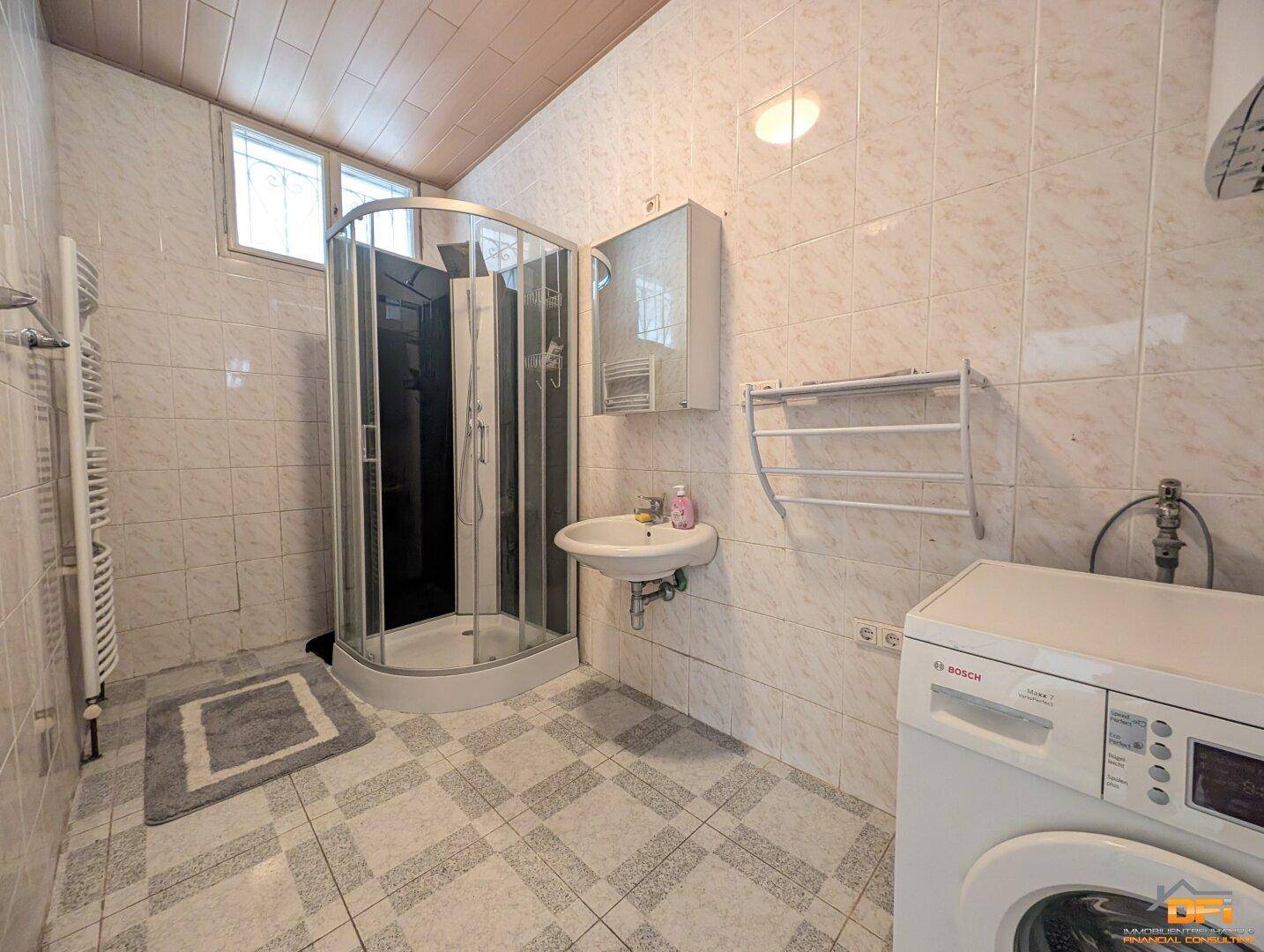 Gefliestes Badezimmer mit Duschkabine, Waschbecken und Waschmaschine.
