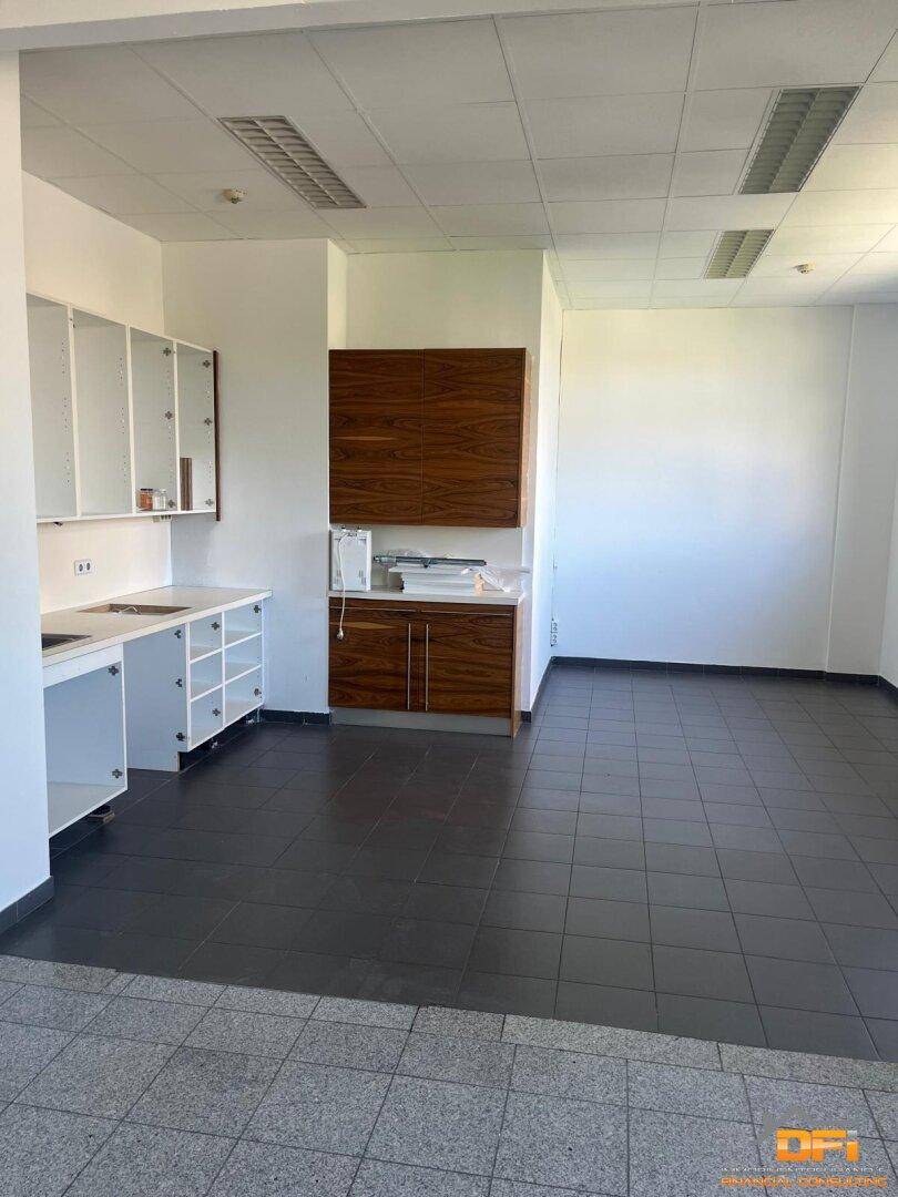 Kleine Küchenzeile mit Holzschränken und Fliesenboden in einem Bürobereich, ideal für Pausen.