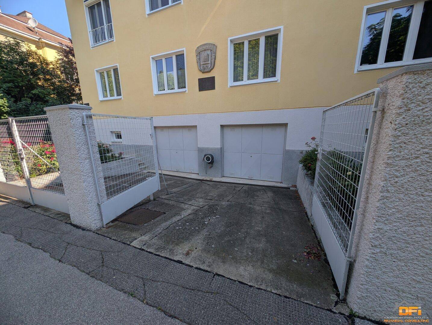 Einfahrt zu zwei Garagen mit geschlossenen Toren an der gelben Gebäudefassade.