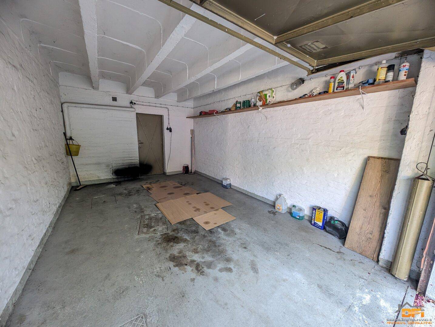 Innenansicht einer Garage mit Betonboden, Regalen und einer Tür an der Rückwand.