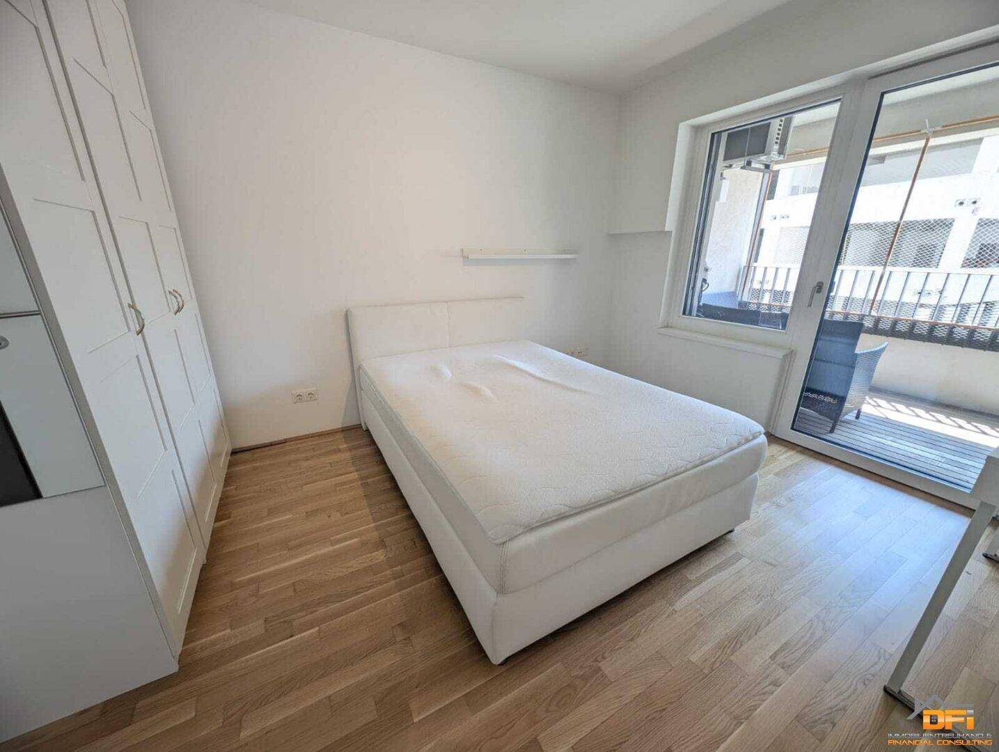 Helles Schlafzimmer mit Balkonzugang, weißem Kleiderschrank und Holzboden.