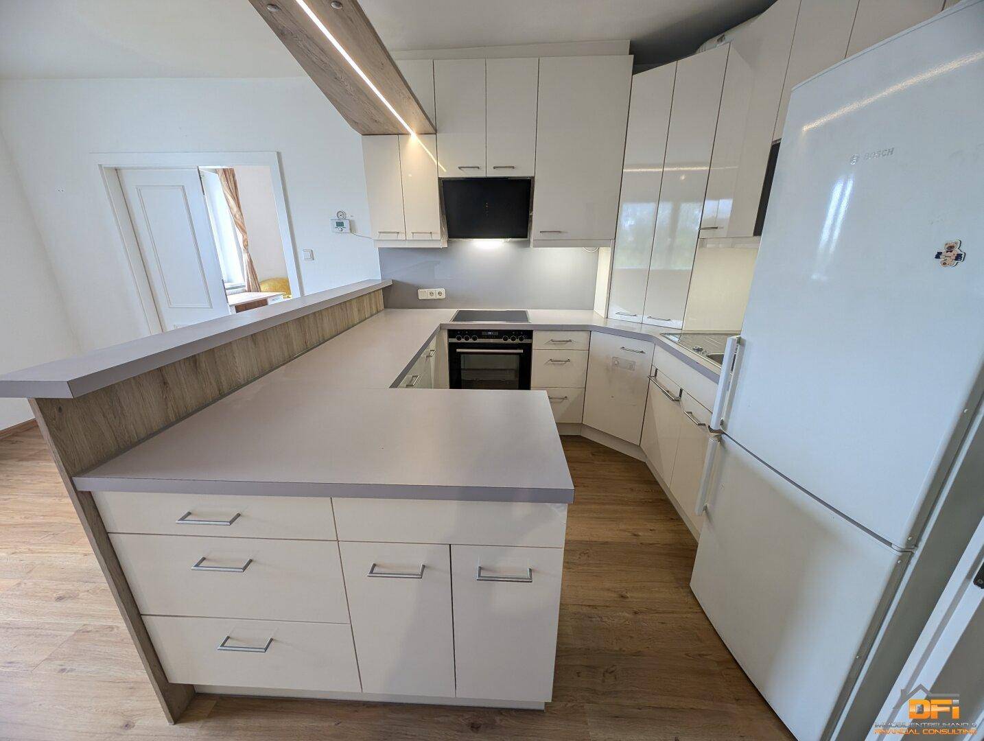 Funktionale Einbauküche mit hellem Laminatboden, integriertem Kühlschrank und Kochfeld.