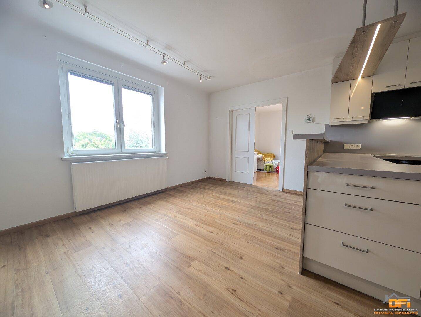 Heller Wohnbereich mit Laminatboden, großem Fenster und Zugang zu einem weiteren Zimmer.