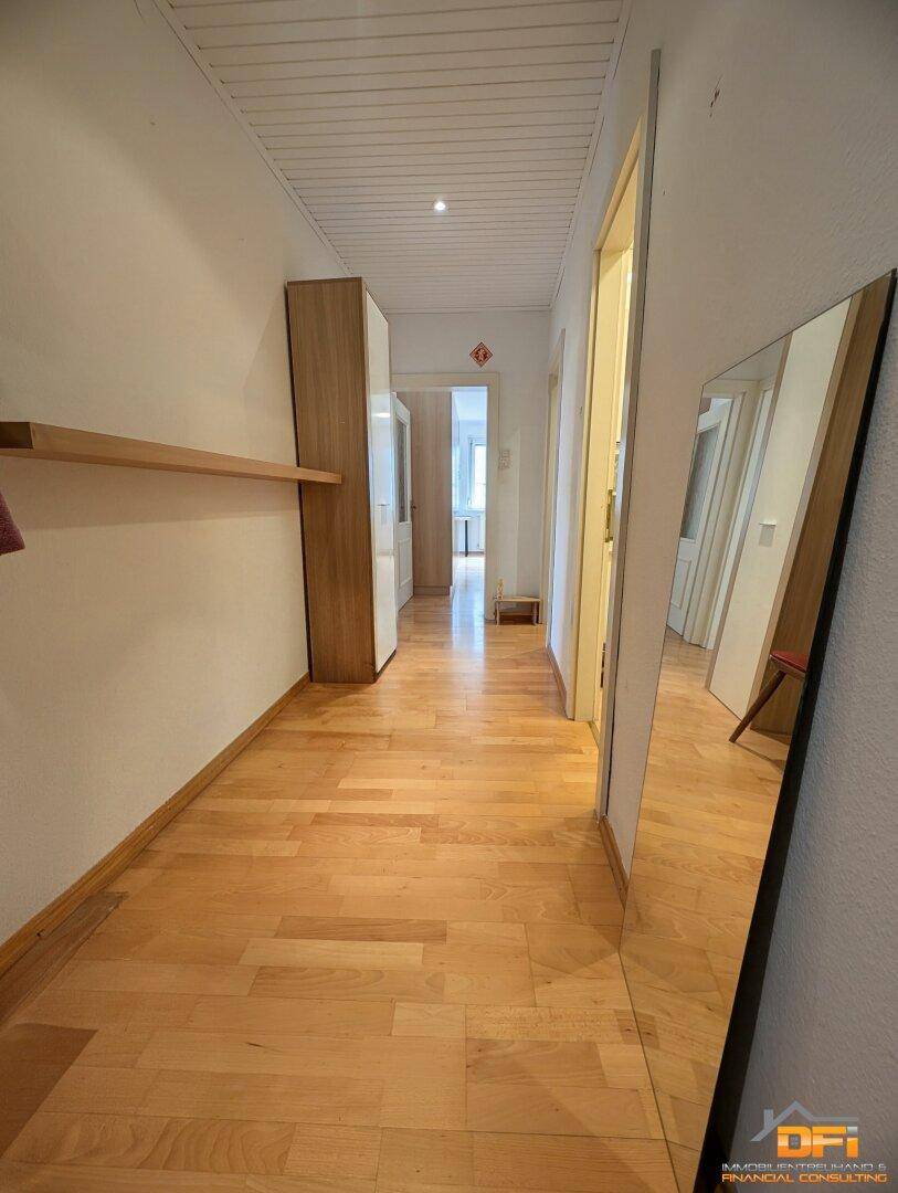 Langer Flur mit Holzparkettboden, Spiegel und Zugang zu den Wohnbereichen.