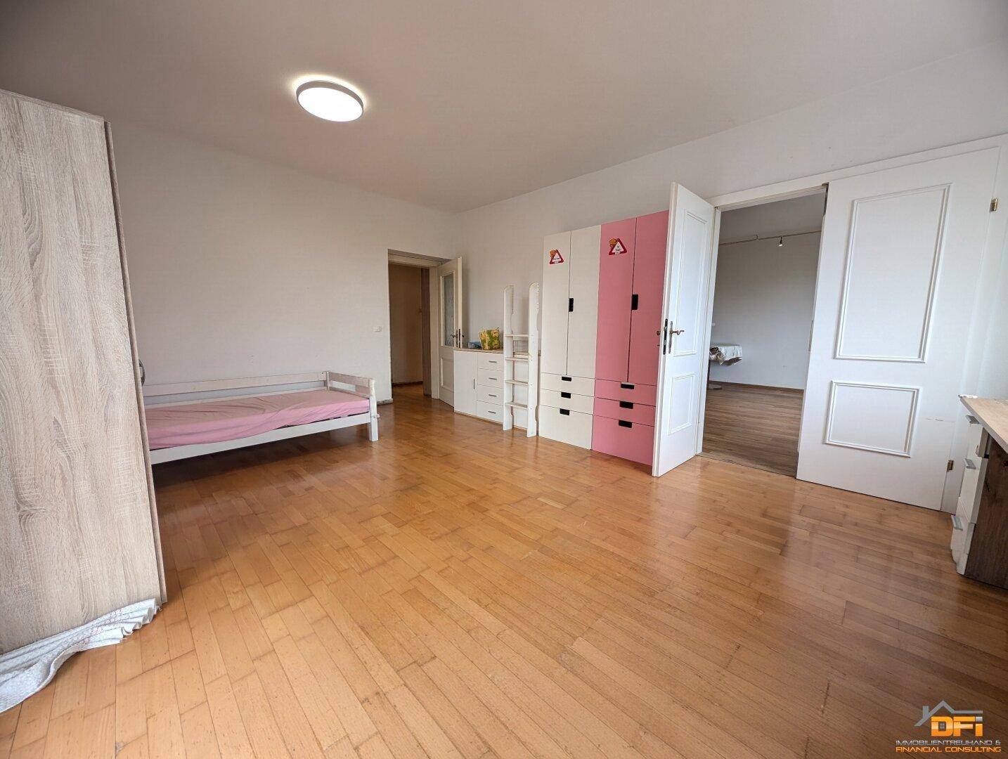 Kinderzimmer mit Parkettboden, bunten Schränken und Zugang zu einem weiteren Raum.