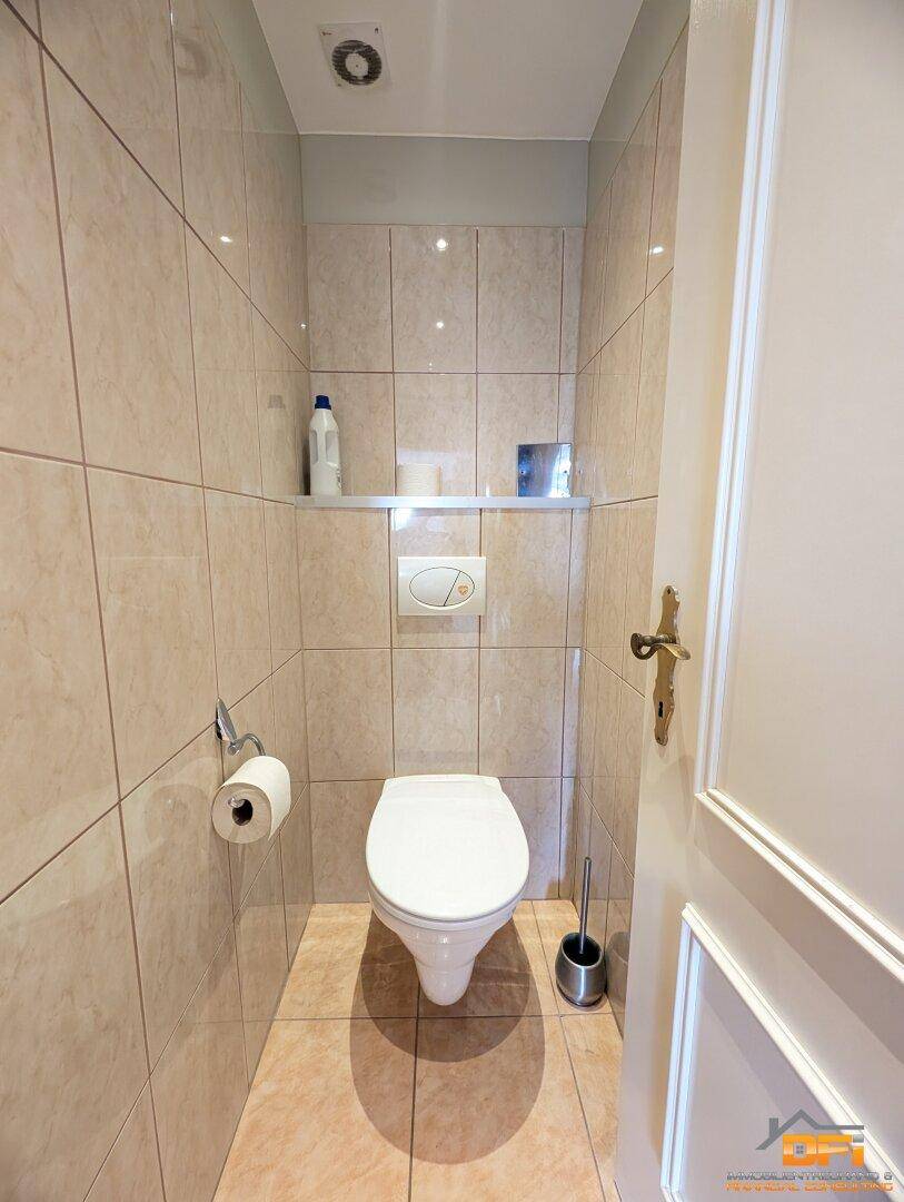 Separate Toilette mit Wand-WC, Fliesenboden und Ablagefläche.