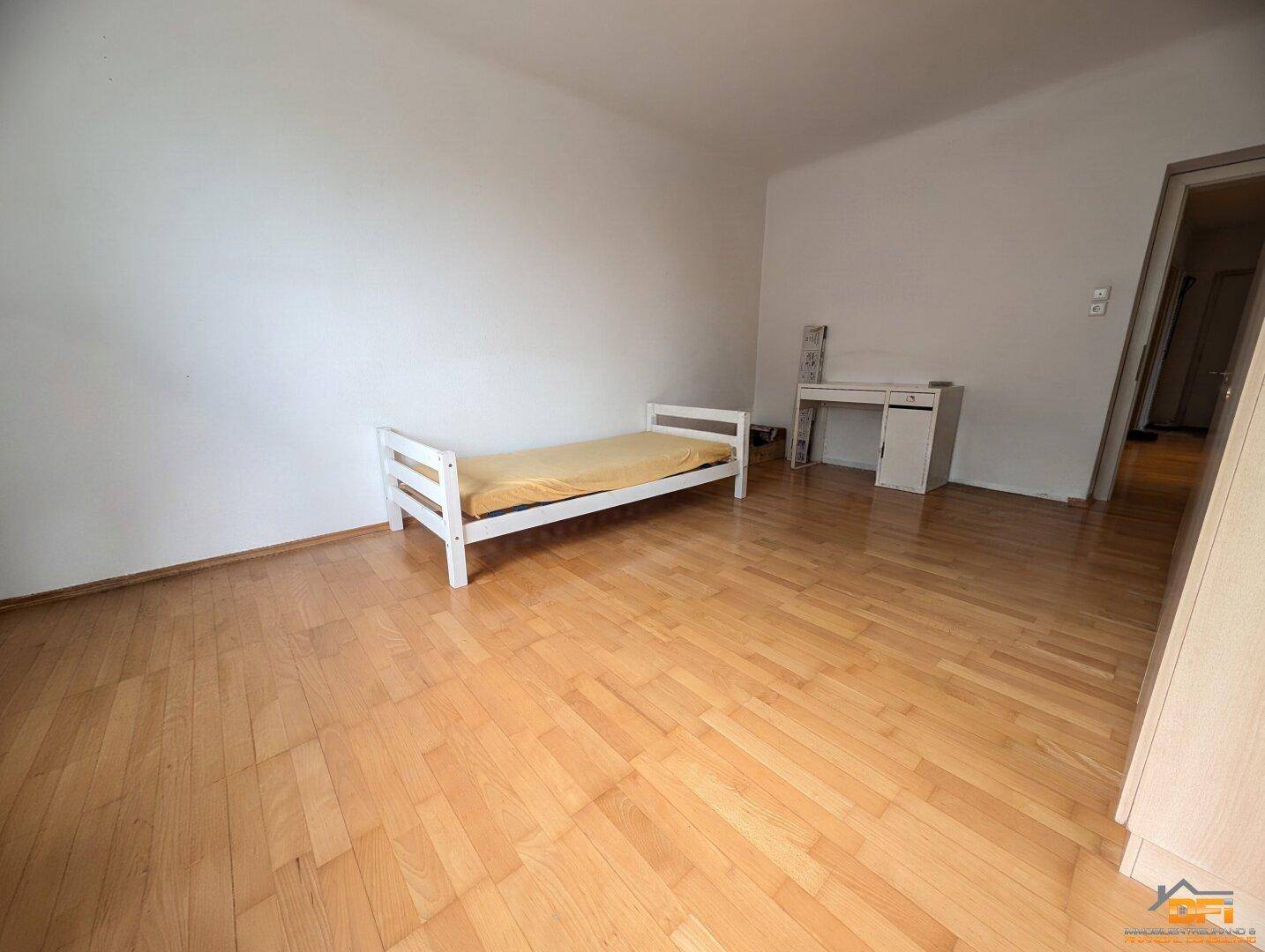 Helles Schlafzimmer mit Parkettboden, Einzelbett und Schreibtisch.