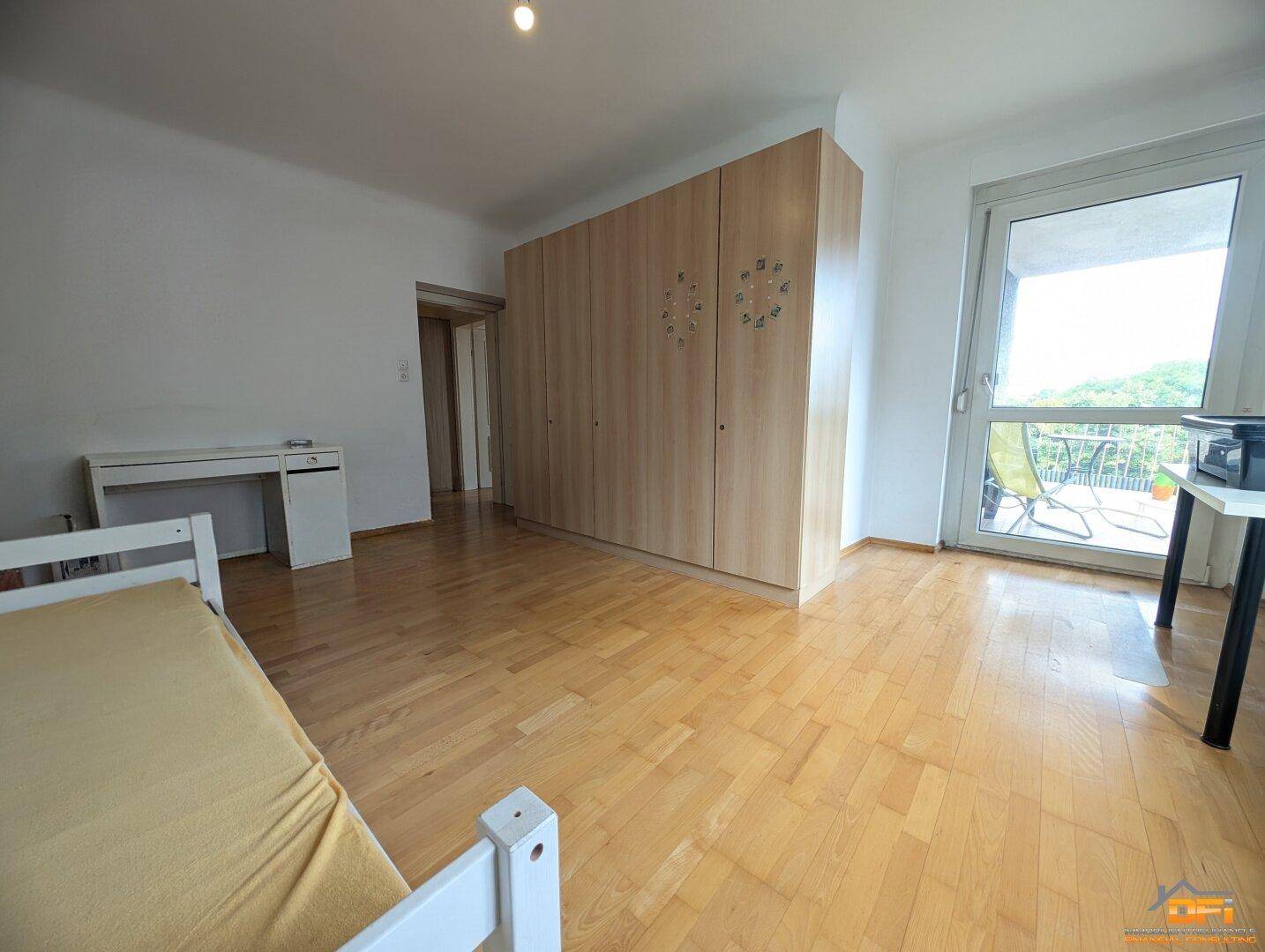 Schlafzimmer mit Parkettboden, großem Kleiderschrank und Balkonzugang.