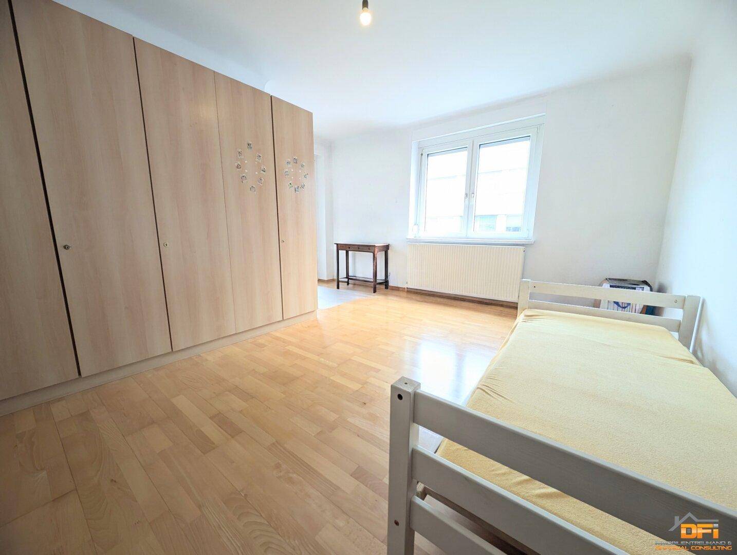 Schlafzimmer mit Parkettboden, Fenster und großem Kleiderschrank.