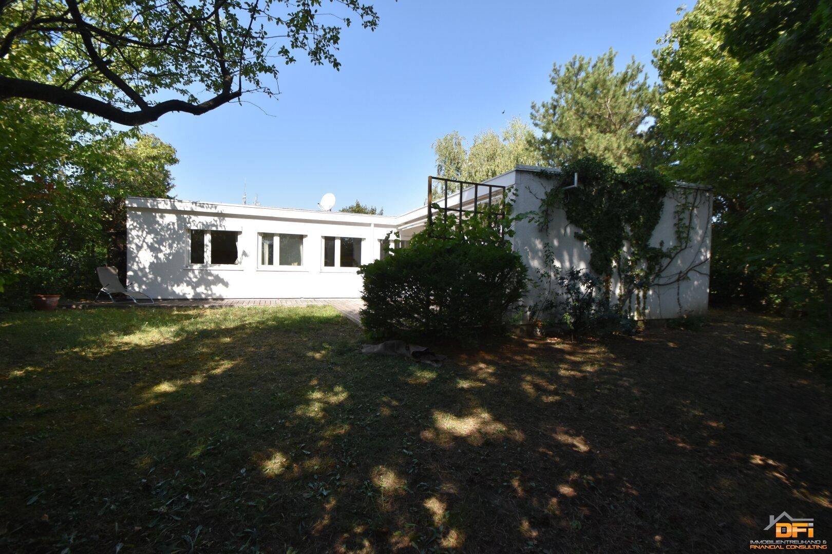 Rückansicht des Hauses mit Garten und viel Grün, umgeben von Bäumen.