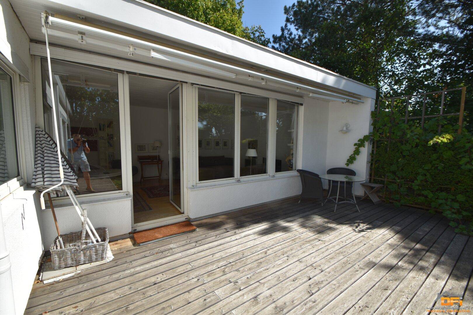 Große Holzterrasse mit Zugang zum Wohnbereich und Blick in den Garten.