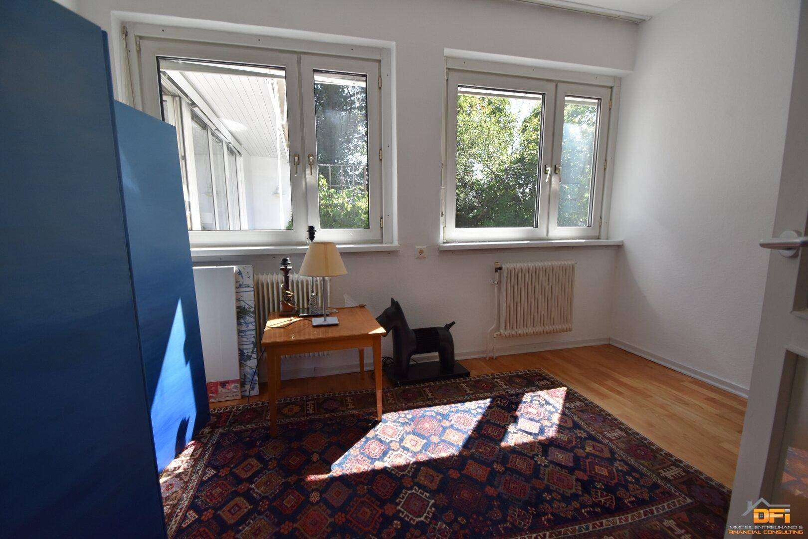 Helles Schlafzimmer mit Holzboden, Teppich und Blick ins Grüne.