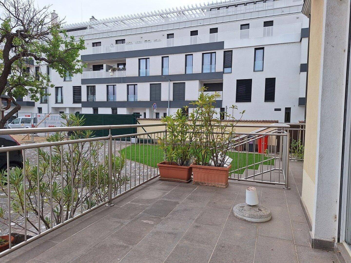 Balkon mit Fliesenboden und Metallgeländer, Blick auf ein modernes Wohngebäude und Grünflächen.