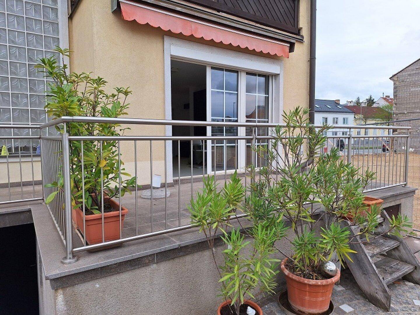 Terrasse mit Pflanzen und Metallgeländer, direkter Zugang zum Garten und Blick auf die Umgebung.