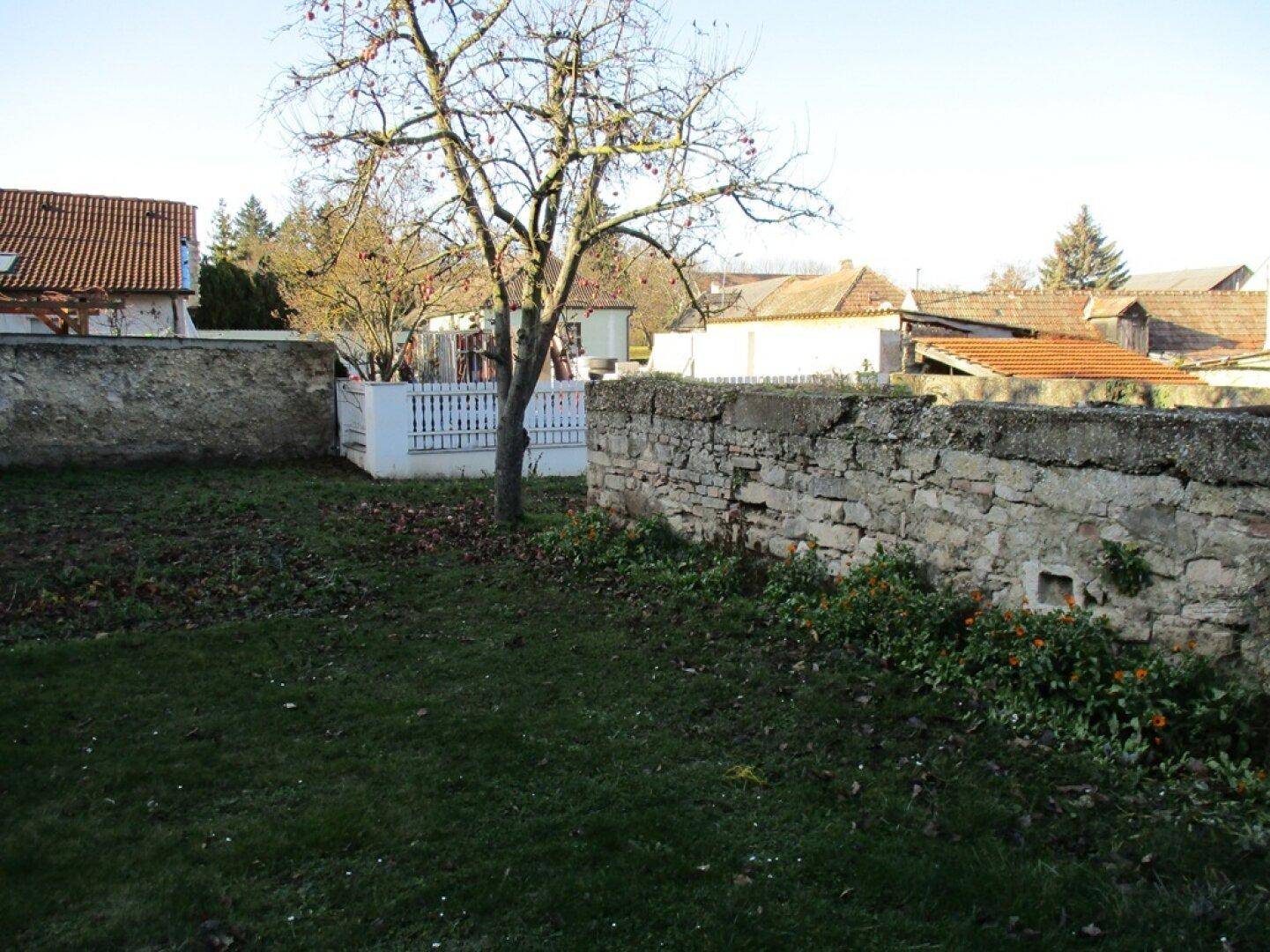 Gartenbereich mit alter Steinmauer, weißem Zaun und kahlem Baum, umgeben von ländlicher Bebauung.