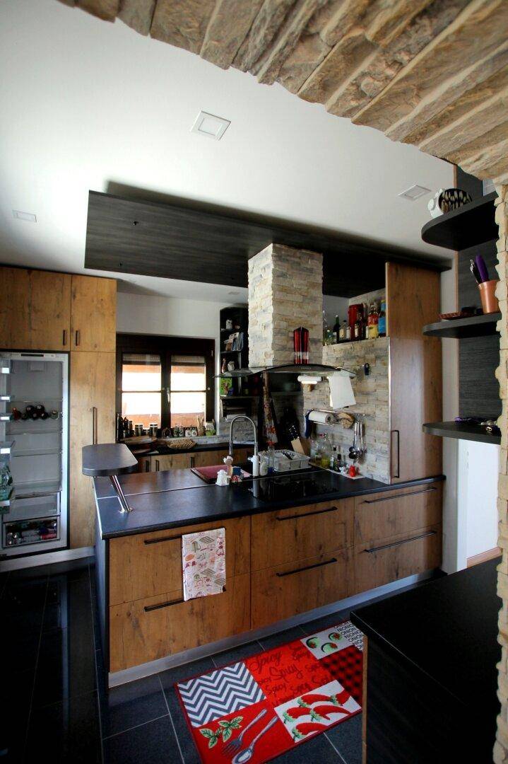 Moderne Holzküche mit dunklen Arbeitsplatten, integrierten Geräten und Steinakzenten an der Wand.