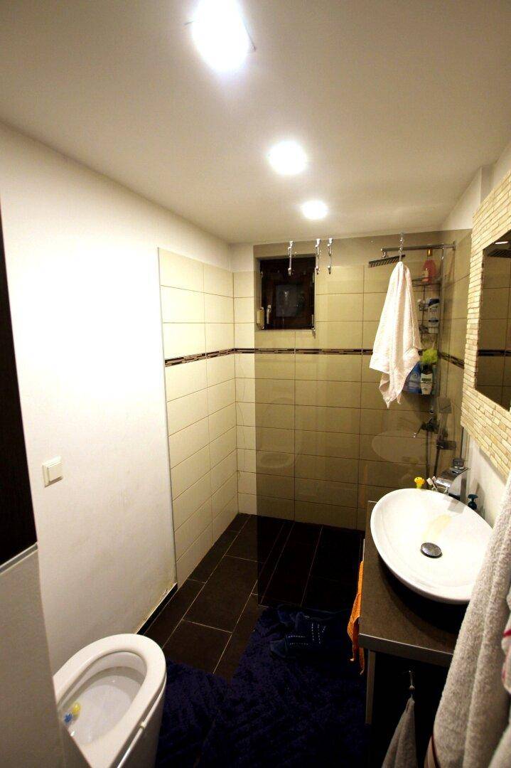 Modernes Badezimmer mit ovalem Waschbecken, Dusche und dunklen Fliesen am Boden.