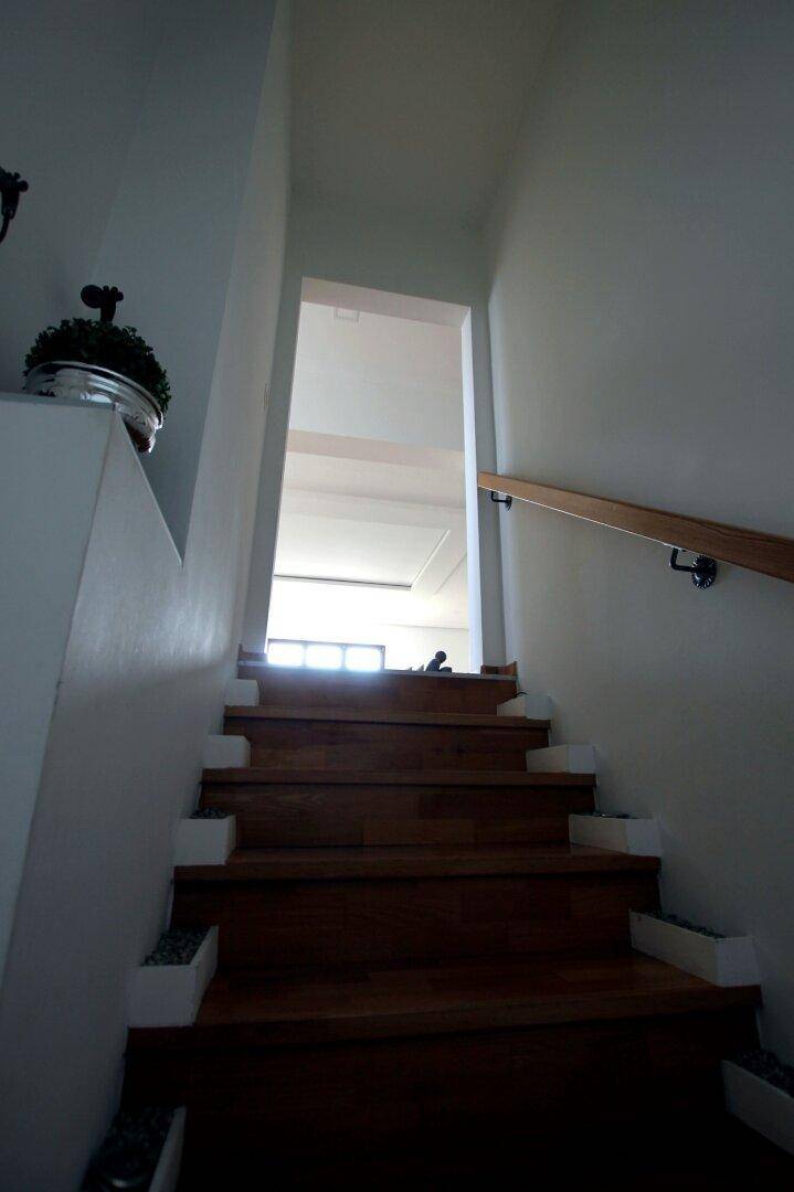 Holztreppe führt in den oberen Bereich des Hauses mit hellem Eingang und Geländer.