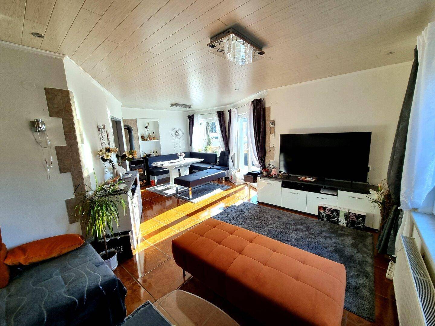 Geräumiger Wohn- und Essbereich mit großem Fernseher, Holzdecke und viel Tageslicht.